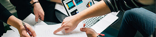 Grafik für die Informationsseiten zu den OBS-Studien. Zu sehen sind die Hände zweier Personen, die gemeinsam an einem Dokument arbeiten. Im Hintergrund ist ein Laptop zu sehen.