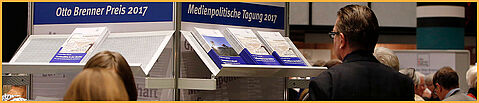 Personen vor einer Auslage mit Publikationen der Otto Brenner Stiftung bei der Medienpolitischen Tagung der OBS 2017